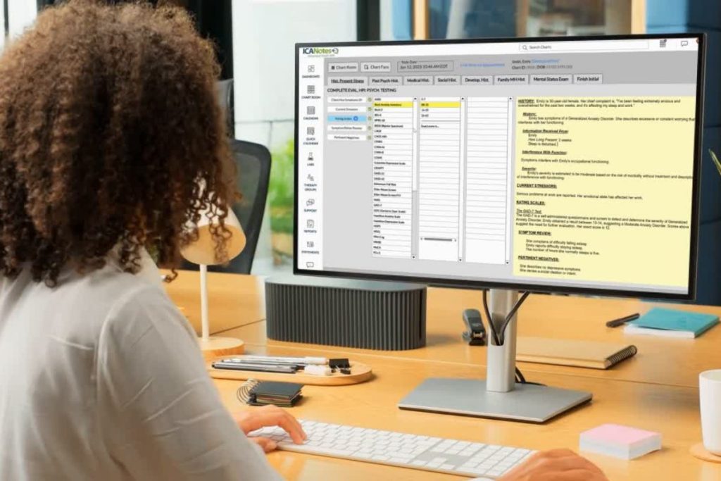 Clinician completing a biopsychosocial assessment in the ICANotes EHR platform on a desktop computer in a modern office setting.