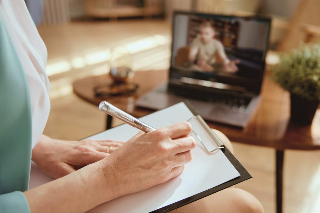 A behavioral health clinician is taking notes during a telehealth session