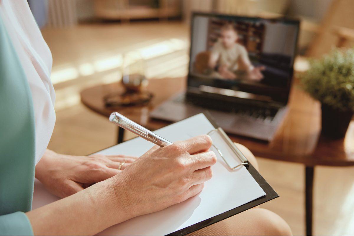 A behavioral health clinician is taking notes during a telehealth session