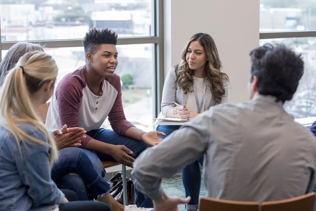 Therapist facilitating a group therapy session while documenting notes using mental health charting software
