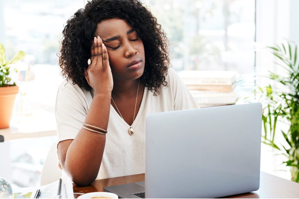 Mental health clinician looking tired and frustrated while working on a laptop, representing common EHR problems and burnout.