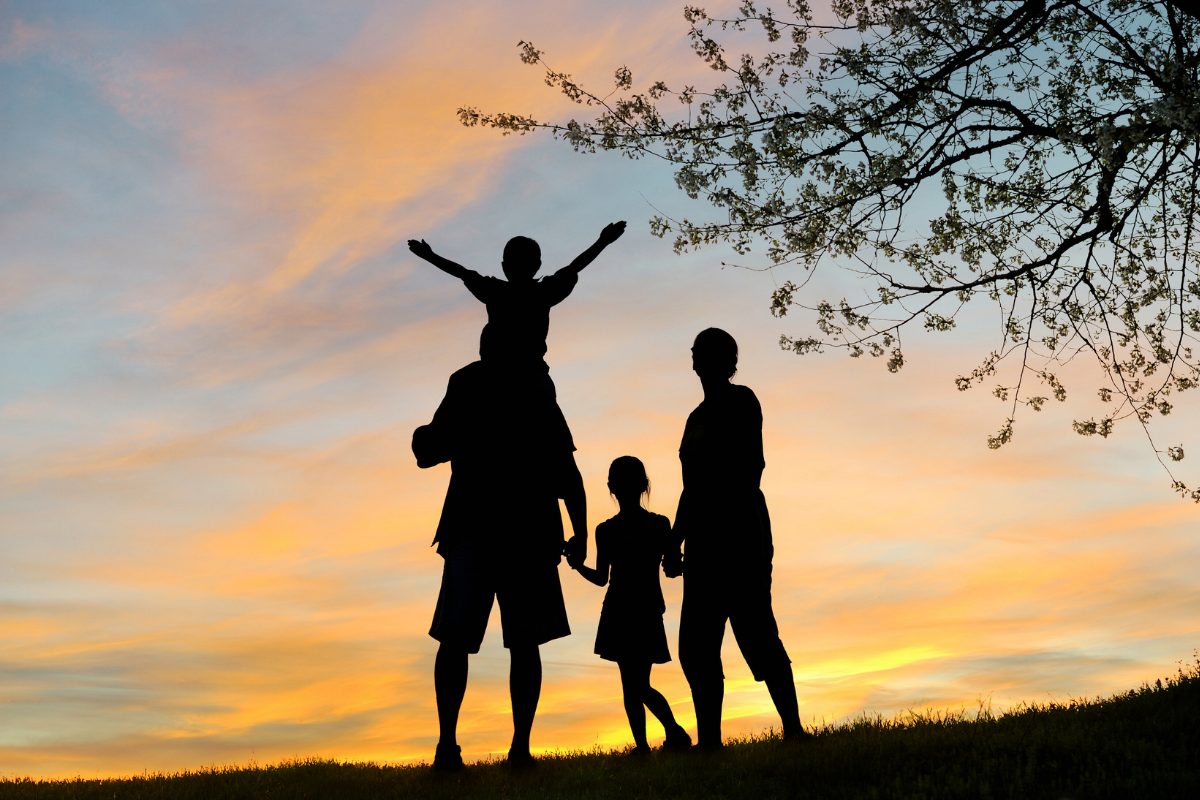 Silhouetted family of four at sunset in nature, with one child on the father’s shoulders, symbolizing connection and strengthened relationships through family therapy interventions.