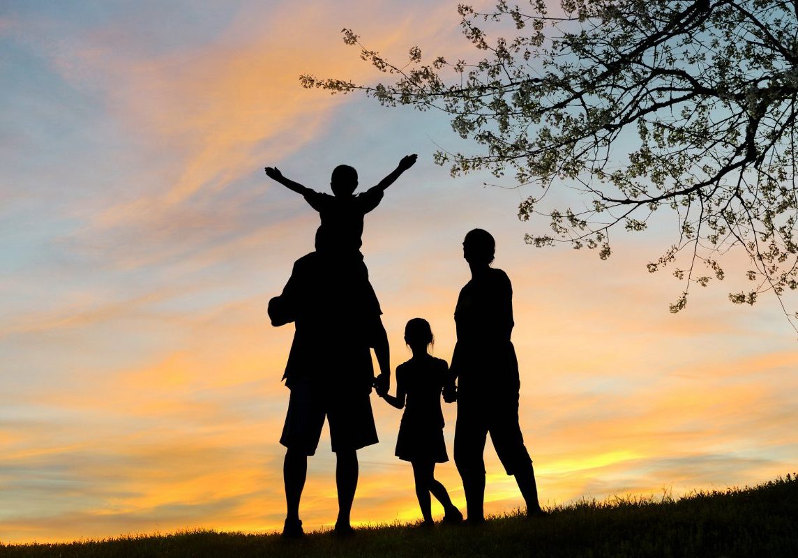 Silhouetted family of four at sunset in nature, with one child on the father’s shoulders, symbolizing connection and strengthened relationships through family therapy interventions.