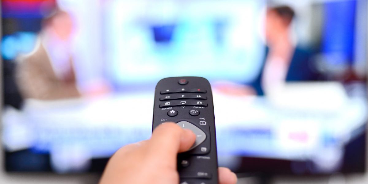 Image of political obsession disorder triggered by constant news exposure on TV Hand holding a TV remote pointed at political news broadcast, symbolizing political obsession disorder