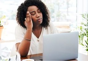 Mental health clinician looking tired and frustrated while working on a laptop, representing common EHR problems and burnout.