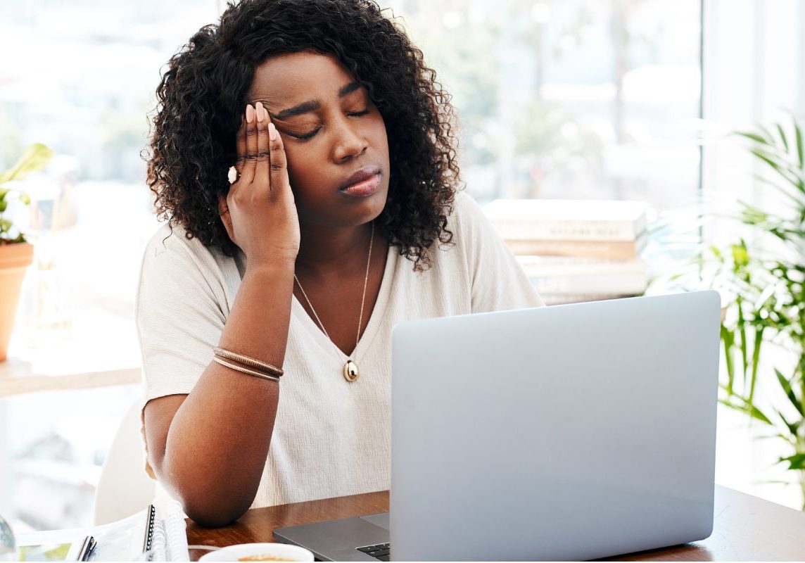 Mental health clinician looking tired and frustrated while working on a laptop, representing common EHR problems and burnout.